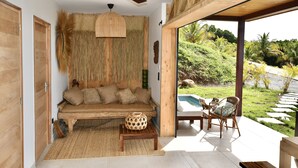 Un intérieur moderne avec un canapé en bois, un ventilateur de plafond et une vue sur un jardin avec une piscine.