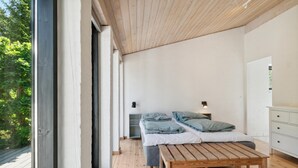 Un dormitorio con techo de madera, una cama con ropa de cama gris, una mesita de noche y un buró con una lámpara.