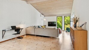 Una sala moderna con techo de madera, un sofá, un televisor y un escritorio con una computadora portátil.