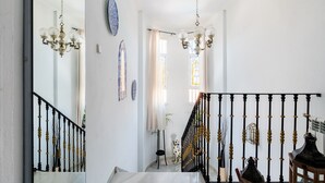 Un escalier avec des balustrades noires, un lustre et un chien debout sur la plateforme.