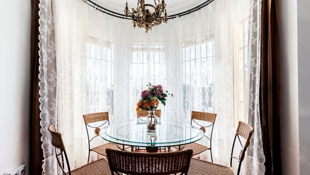 Une table ronde en verre, des chaises en osier, un vase rempli de fleurs et un lustre.