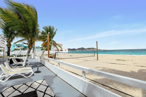 A beachside balcony with lounge chairs, a volleyball net, and a view of the beach and ocean.