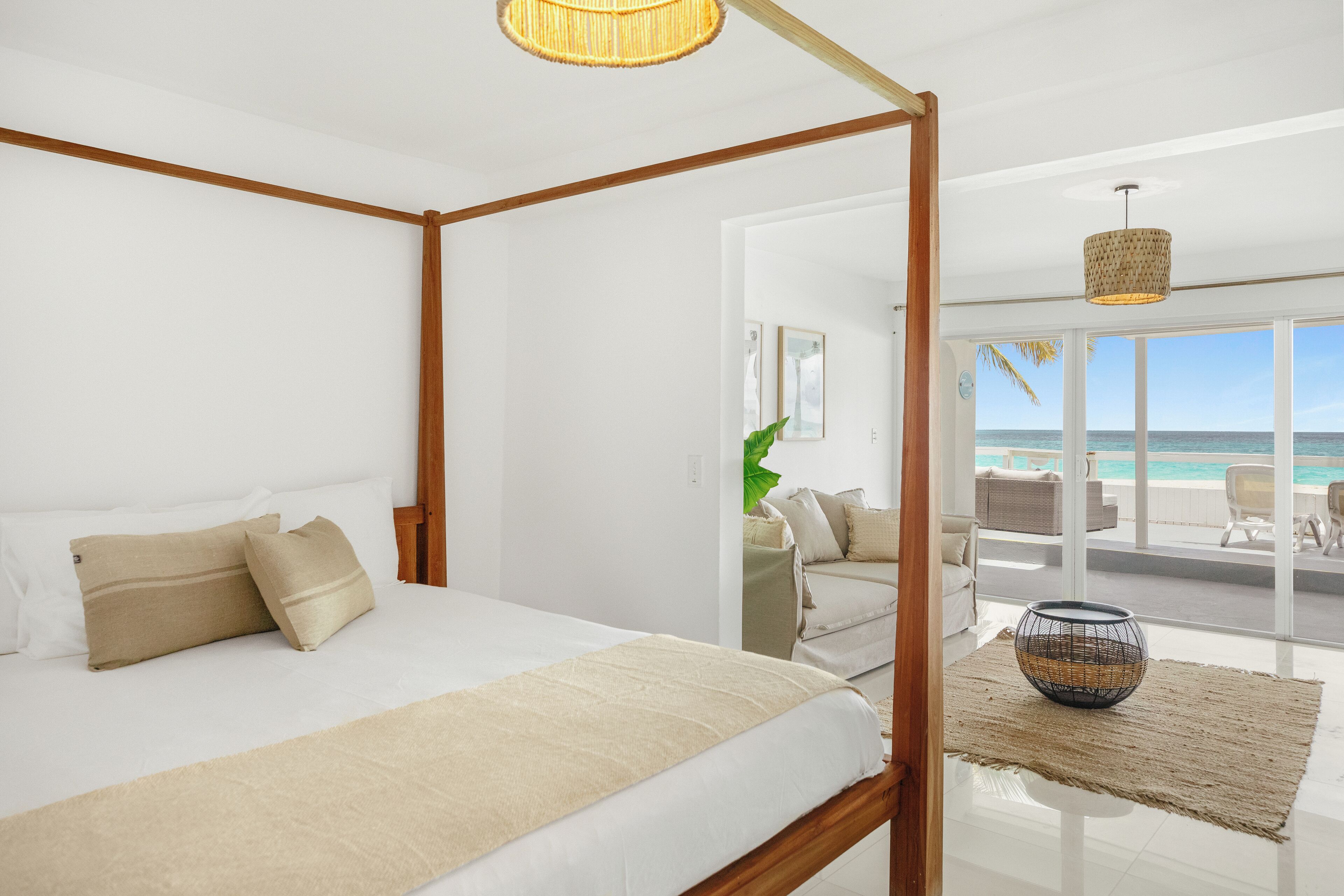 A bedroom with a four-poster bed, a view of the beach, and a balcony with wicker furniture.