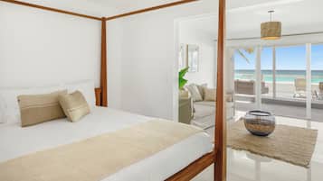 A bedroom with a four-poster bed, a view of the beach, and a balcony with wicker furniture.