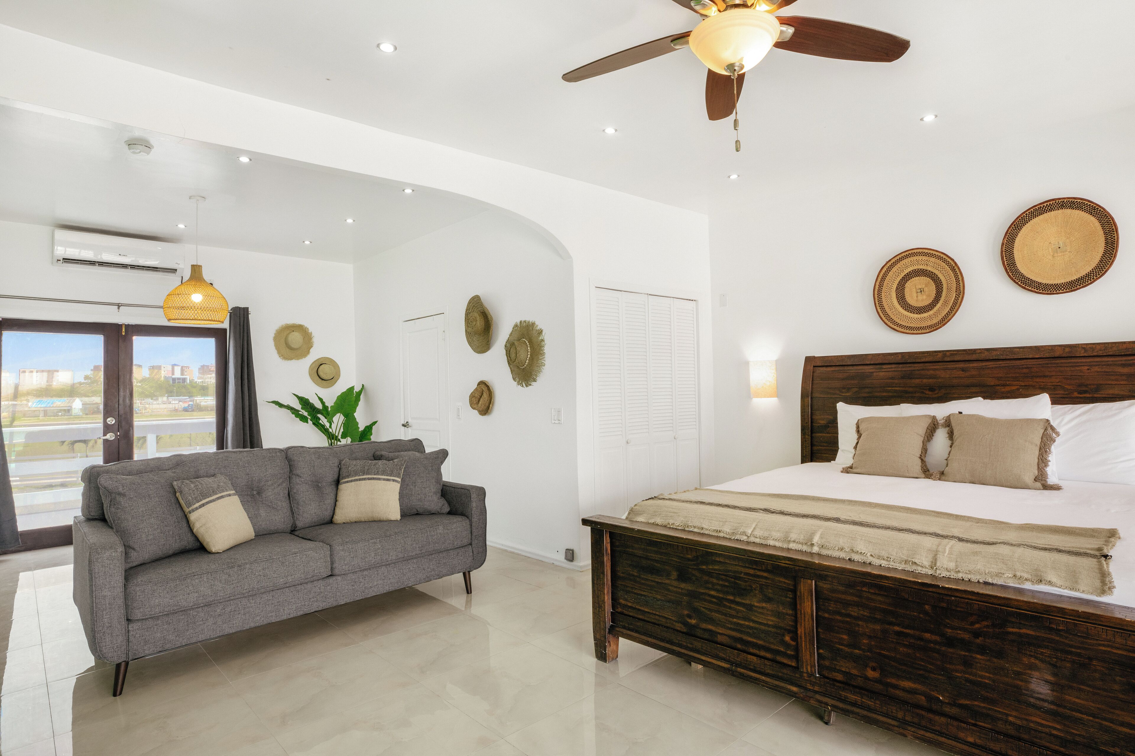 A modern bedroom with a large bed, a grey sofa, and a ceiling fan.