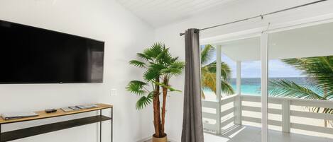Una habitación moderna con televisión de pantalla plana, una mesita de madera, una palma en maceta y un balcón con vistas al océano.
