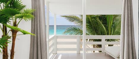 A balcony with a white railing, a bed, and a view of the ocean.