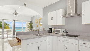 A modern kitchen with white cabinets, a stainless steel range hood, a microwave, and a kettle. - Cocovaa (Simpson Bay)