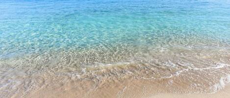 A clear beach with calm waters, a sandy shore, and a distant cruise ship.