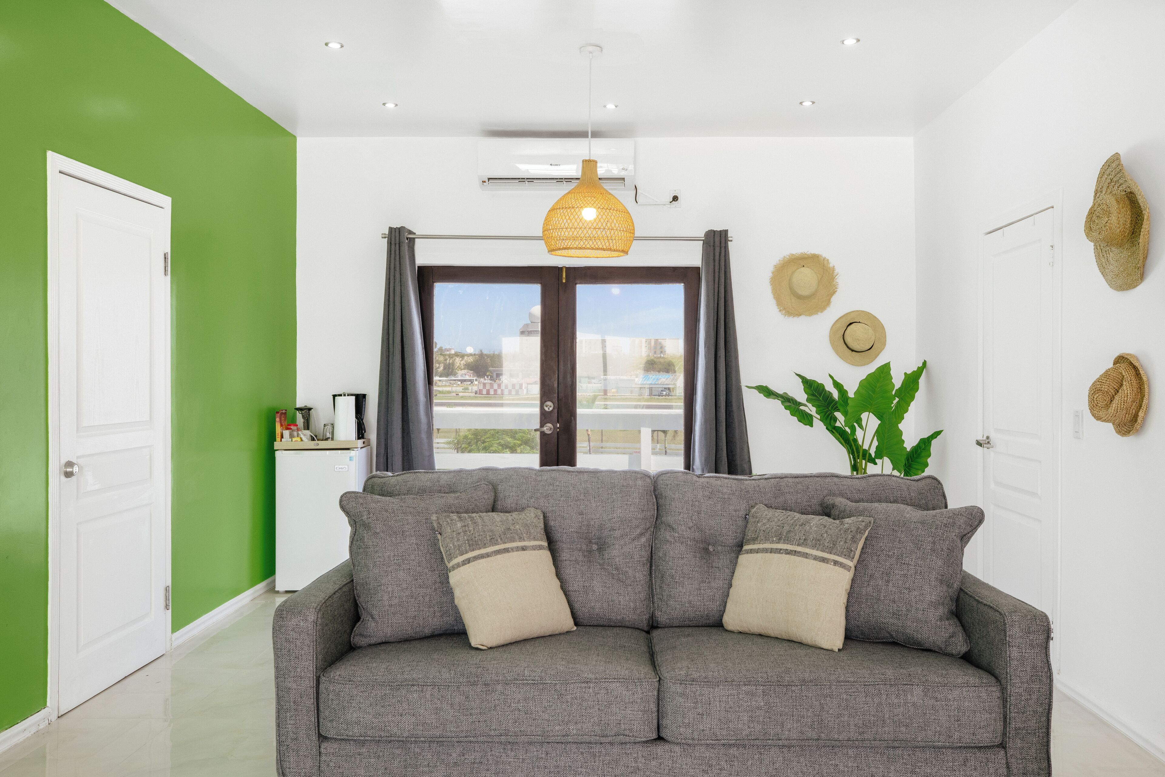A modern living room with a grey sofa, a hanging woven light fixture, and a view through large windows.