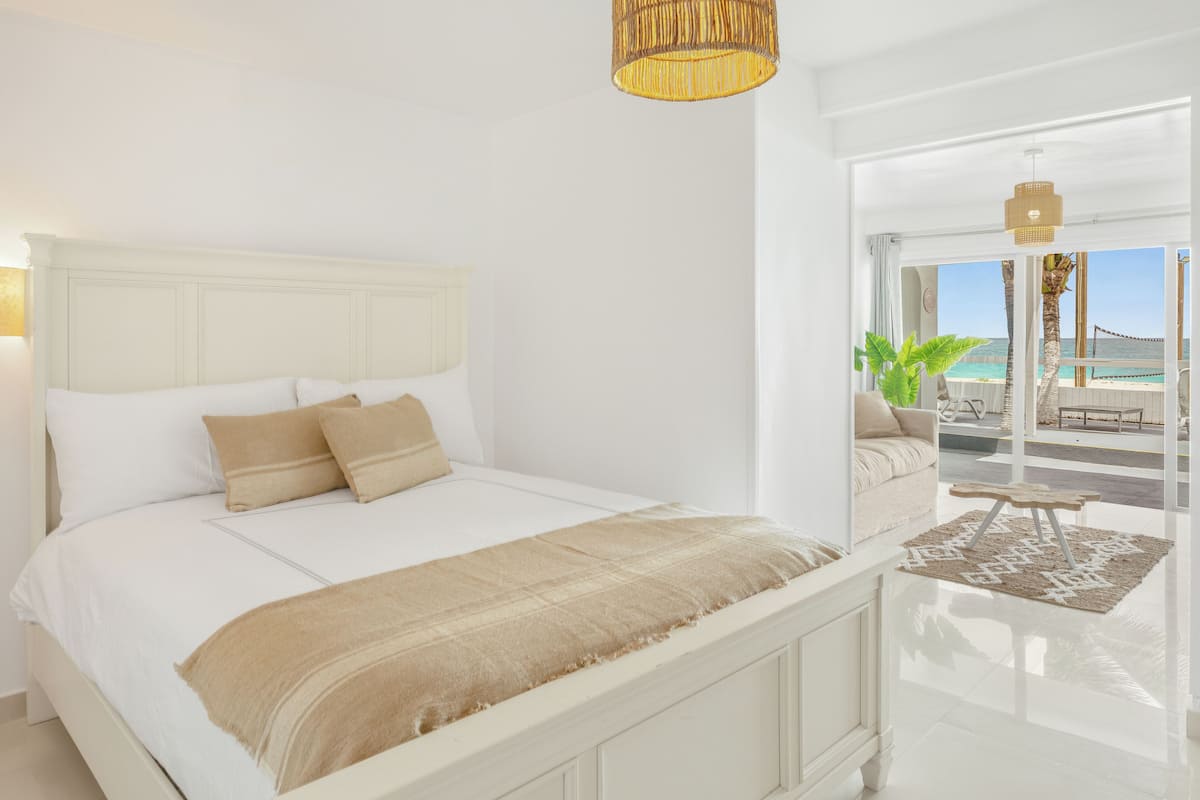 A bedroom with a large bed, a view of the beach, and a balcony with a table and chairs.