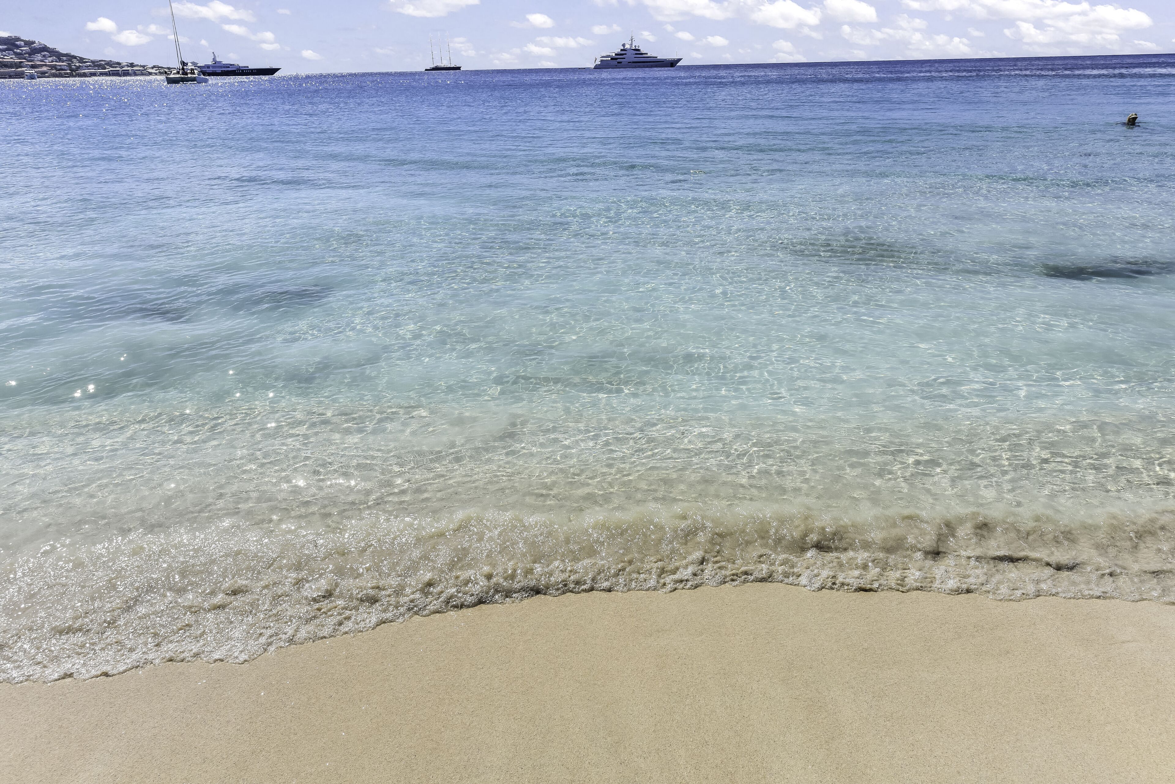A beach with clear water, a sandy shore, and two boats in the distance.