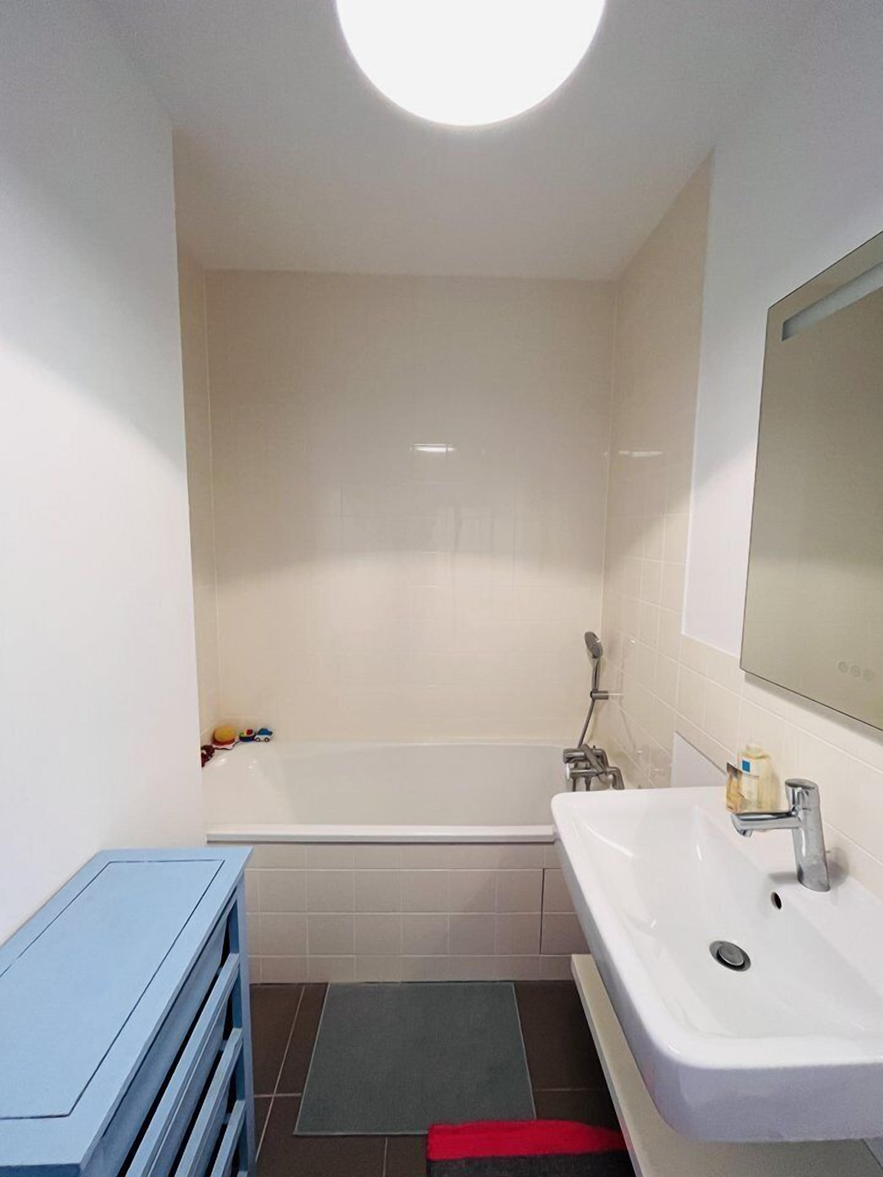A modern bathroom with a white bathtub, a large mirror, and a blue vanity.