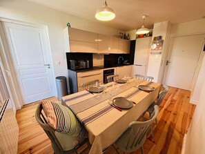 Une cuisine compacte avec une table à manger pour quatre personnes, équipée des appareils de base et d’une poubelle.
