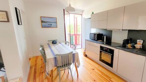 A modern kitchen with wooden flooring, a dining table with chairs, a built-in oven, and a black countertop with a sink. - La riviéra" apartment. (HOSSEGOR)