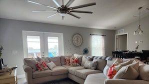 A modern living room with a sectional sofa, a ceiling fan, and a dining area with a table and chairs. - Cape Coral Pool/Spa Home (Cape Coral)