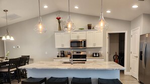 A modern kitchen with white cabinets, a large island with bar stools, a microwave, and a stainless steel refrigerator. - Cape Coral Pool/Spa Home (Cape Coral)