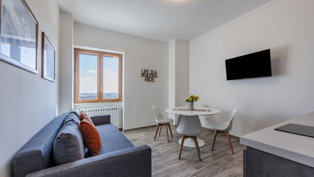 Un salon moderne comprenant un canapé, une table à manger avec des chaises, un téléviseur fixé au mur et une fenêtre donnant sur un beau paysage.