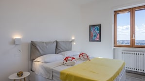 Une chambre d’hôtel avec un lit, une fenêtre donnant sur un paysage agréable, un radiateur et une petite table sur laquelle est posé un vase.