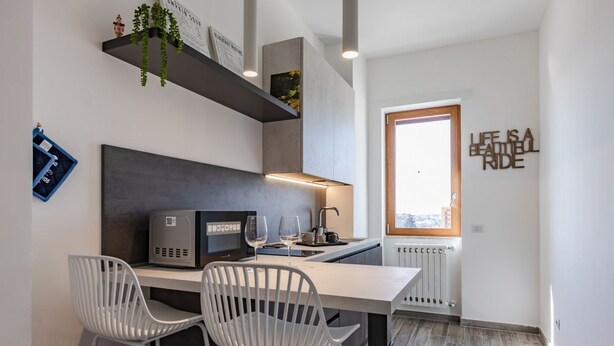 A modern kitchen with a built-in microwave, two white chairs, and a window with a view.