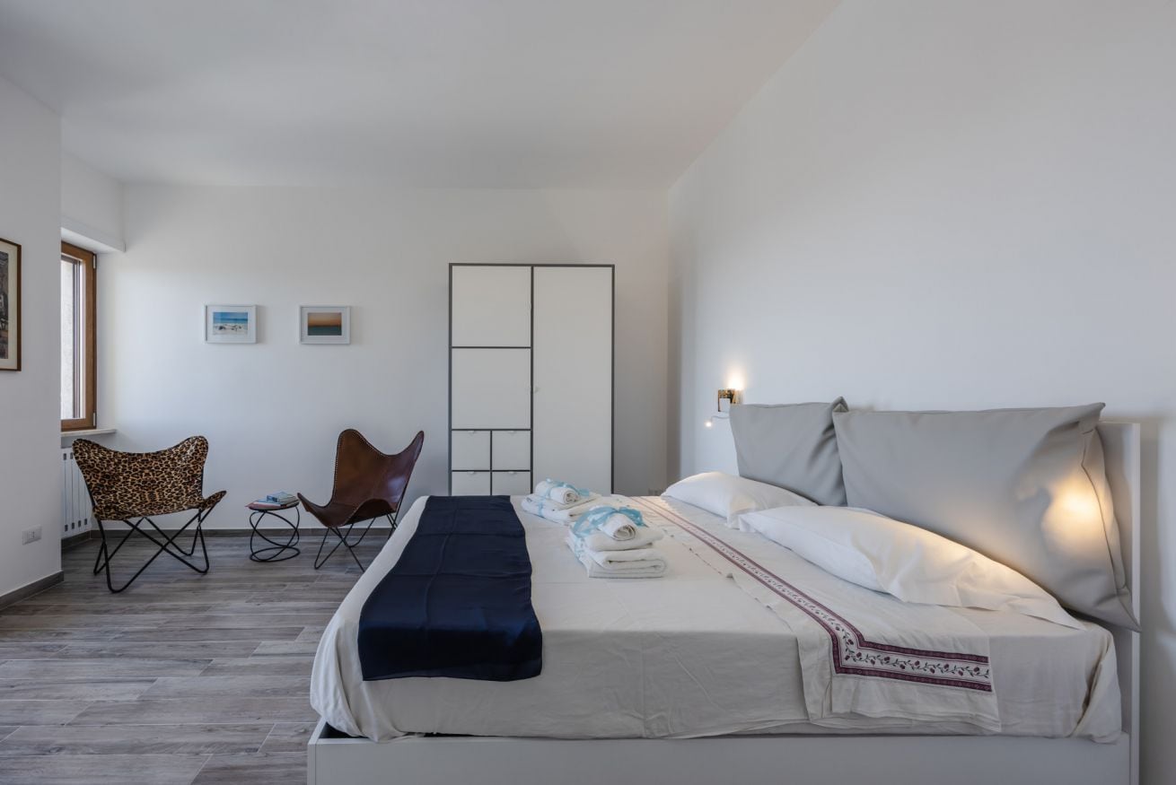 Une chambre d’hôtel avec un lit, deux chaises, une table de chevet, une armoire et une fenêtre.