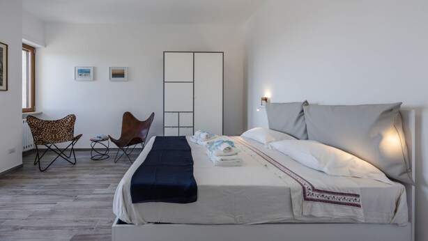 A hotel room with a bed, two chairs, a side table, a wardrobe, and a window.