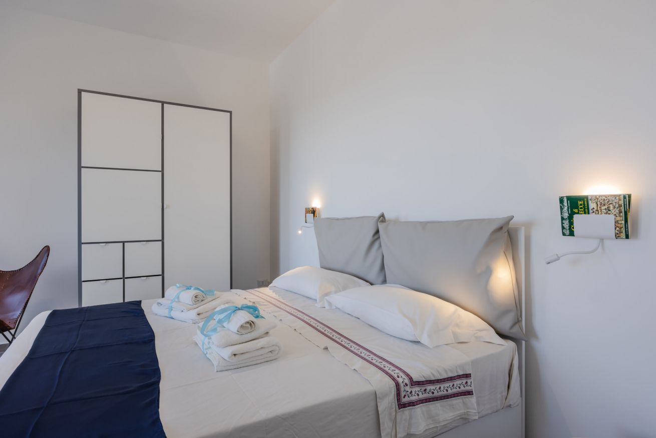 A hotel room with a bed, a wardrobe, a chair, and a wall-mounted light fixture.