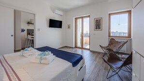A hotel room with a bed, a TV, a balcony, and a chair.