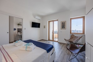 A hotel room with a bed, a TV, a balcony, and a chair.