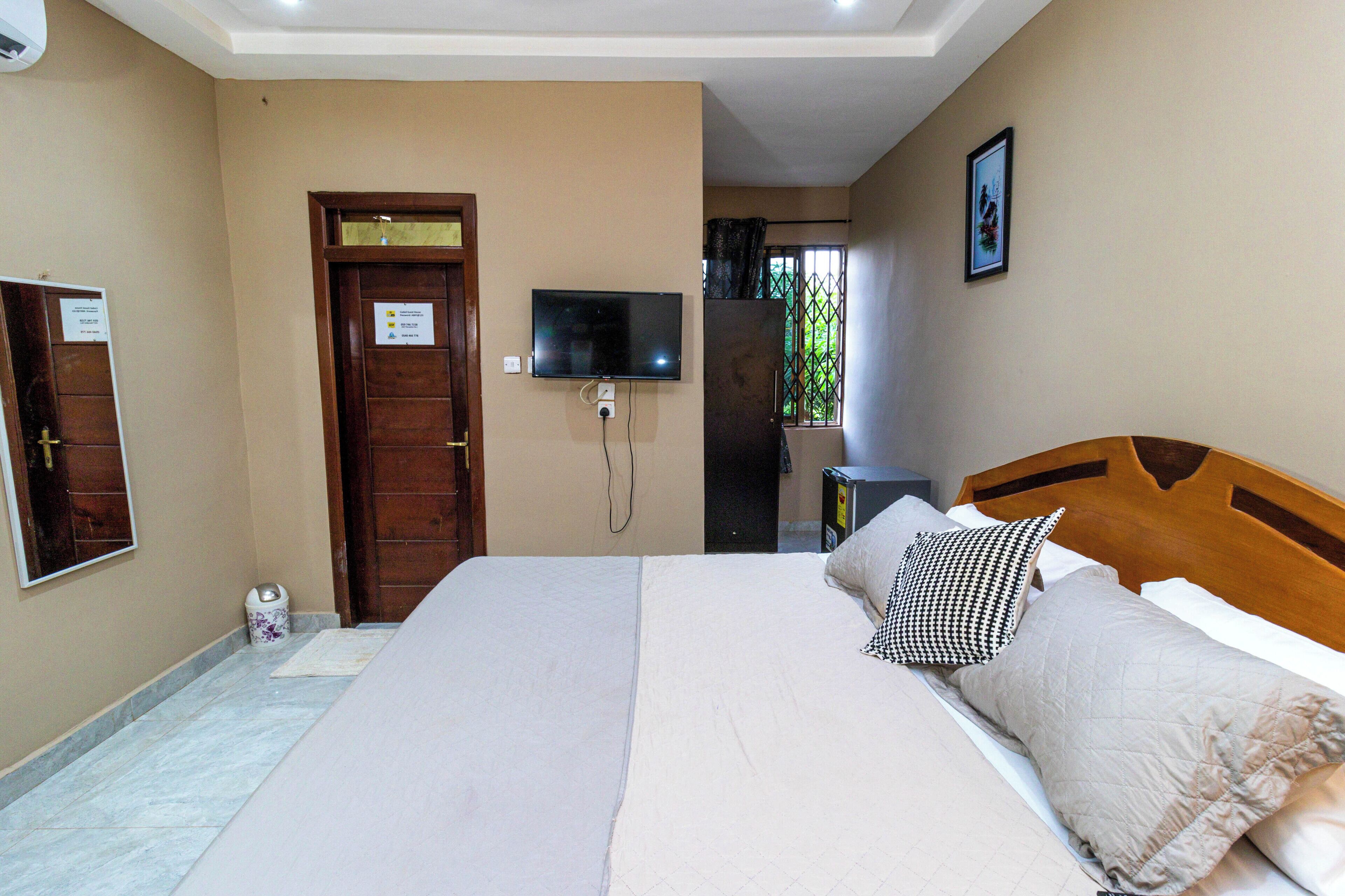 Habitación de hotel con una cama, un televisor montado en la pared y una puerta con un cartel.