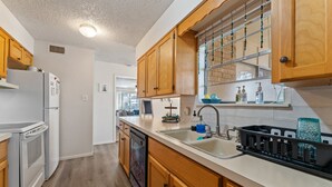 A modern kitchen with wooden cabinets, a built-in dishwasher, and a large window with decorative beads. - The Lake Escape @Brownwood (Brownwood)