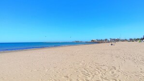 Une vaste plage de sable fin, sous un ciel bleu dégagé et une mer calme.
