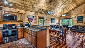 A wooden cabin interior with a kitchen, dining area, and living room. - Family Retreat - HotTub! Theater! FirePit! Wifi! Grill! Jacuzzi in both bedrooms (Pigeon Forge)