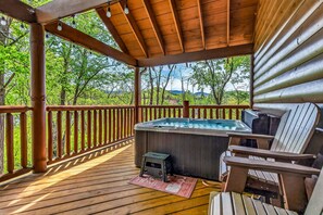 Eine Holzterrasse mit Whirlpool, Adirondack-Stühlen und Blick auf Bäume und Hügel.