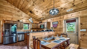 A wooden cabin interior with a dining area, kitchen, and a sign indicating 'Mom's Diner Open 24 Hours.' - Family Retreat - HotTub! Theater! FirePit! Wifi! Grill! Jacuzzi in both bedrooms (Pigeon Forge)