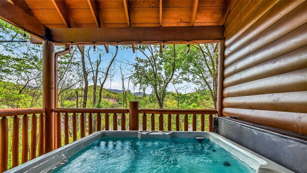 A hot tub on a wooden deck with a view of green trees and hills. - Family Retreat - HotTub! Theater! FirePit! Wifi! Grill! Jacuzzi in both bedrooms (Pigeon Forge)