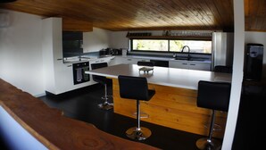A modern kitchen with a central island, bar stools, and a view of the outdoors.