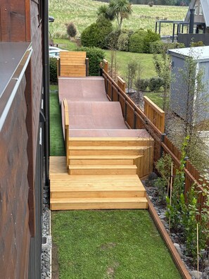 Une terrasse en bois avec des marches menant à une maison, le tout entouré d’un jardin avec de la pelouse et des plantes.