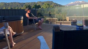 A wooden deck with a hot tub, seating area, and a glass enclosure.