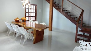 A dining area with a wooden table and white chairs, a staircase, and a window with a view. - CASA VIVA MILAGRES (São Miguel dos Milagres)