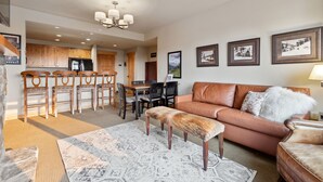 A spacious living area with a brown leather sofa, a wooden dining table with chairs, and a kitchen in the background. - Freshly updated 3 bedroom ski in and out Morning Eagle condo (Whitefish)