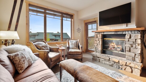 A cozy living room with a stone fireplace, leather furniture, and a large window offering a view of the city. - Freshly updated 3 bedroom ski in and out Morning Eagle condo (Whitefish)