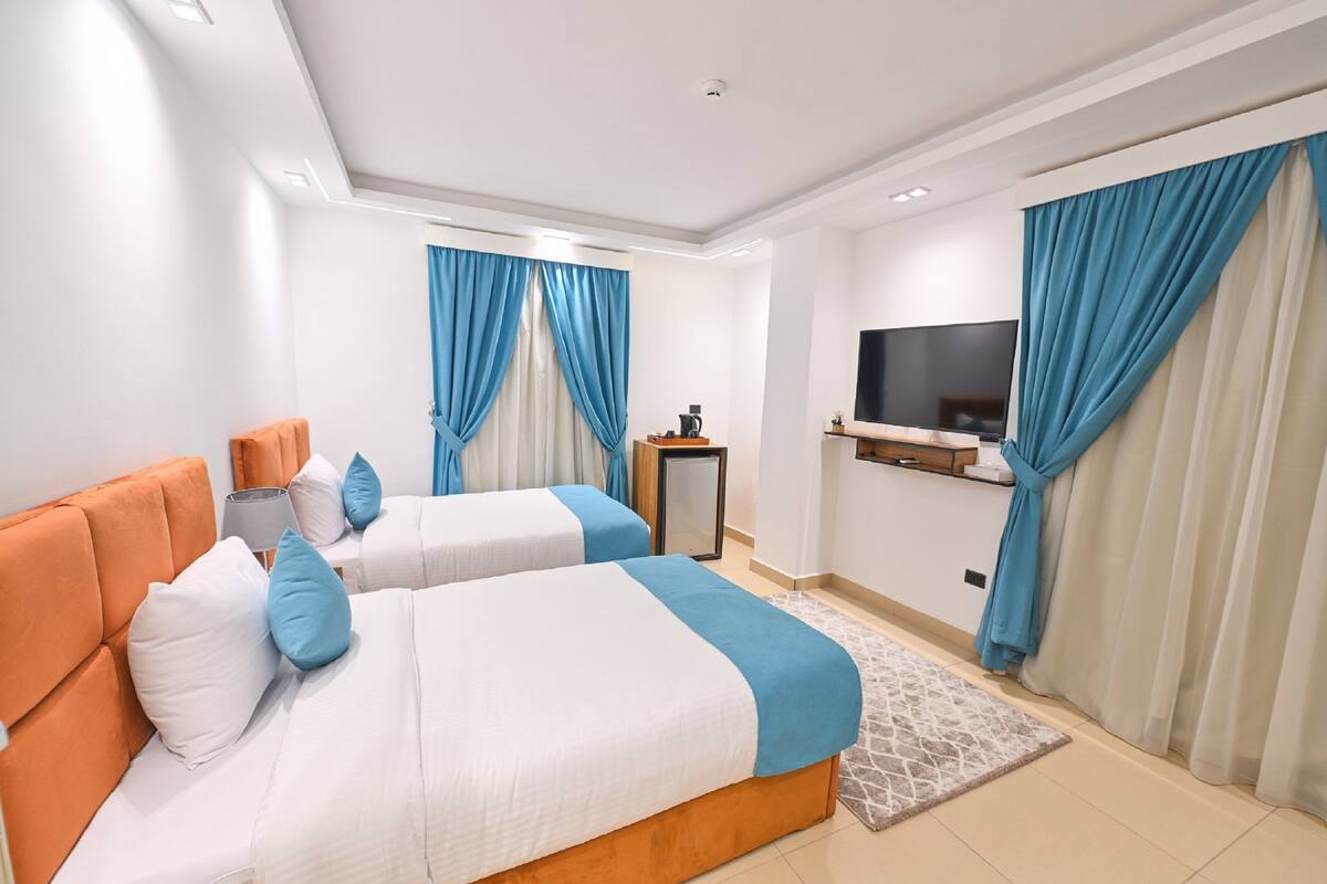 A hotel room with two beds, a TV, and a desk with a computer.