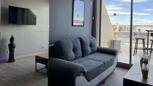 A modern living room with a grey sofa, a flat-screen TV, and a Buddha statue. - Studio Sensuel (LE CAP D'AGDE)