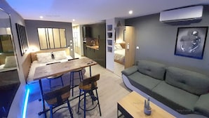 A modern living room with a sofa, a dining table with chairs, and a kitchen area in the background. - Studio Sensuel (LE CAP D'AGDE)