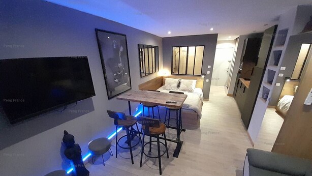 A modern living room with a flat-screen TV, a wooden dining table, bar stools, a sofa, and a coffee table. - Studio Sensuel (LE CAP D'AGDE)