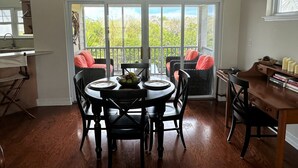 A dining area with a round table, black chairs, and a view through a glass door to a balcony. - Beautiful, centrally located, short drive to beaches and stores. (George Town)