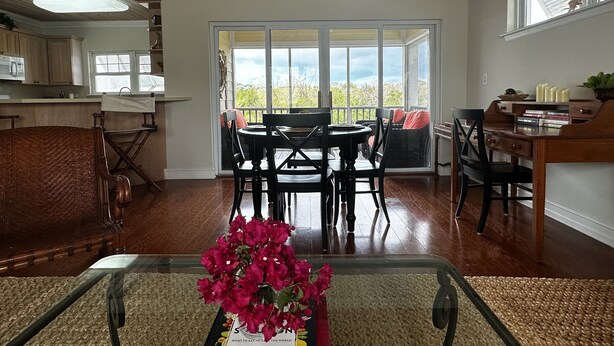 A dining area with a table and chairs, a kitchen in the background, and a view through large windows. - Beautiful, centrally located, short drive to beaches and stores. (George Town)