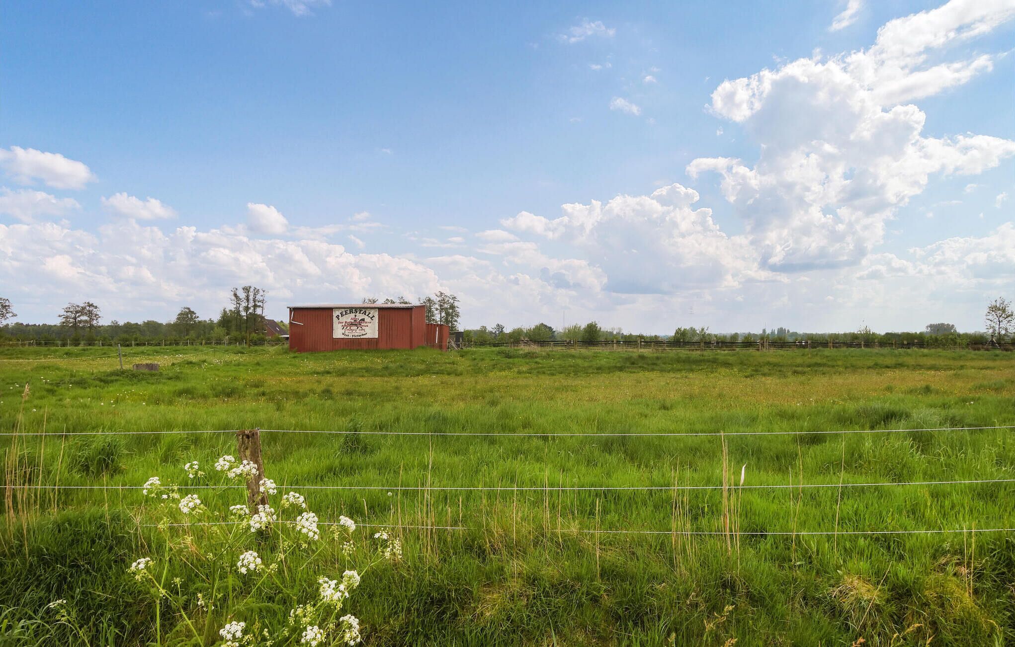 A rural landscape with a red building labeled "Beerstall" in the distance, surrounded by green fields and a clear sky.