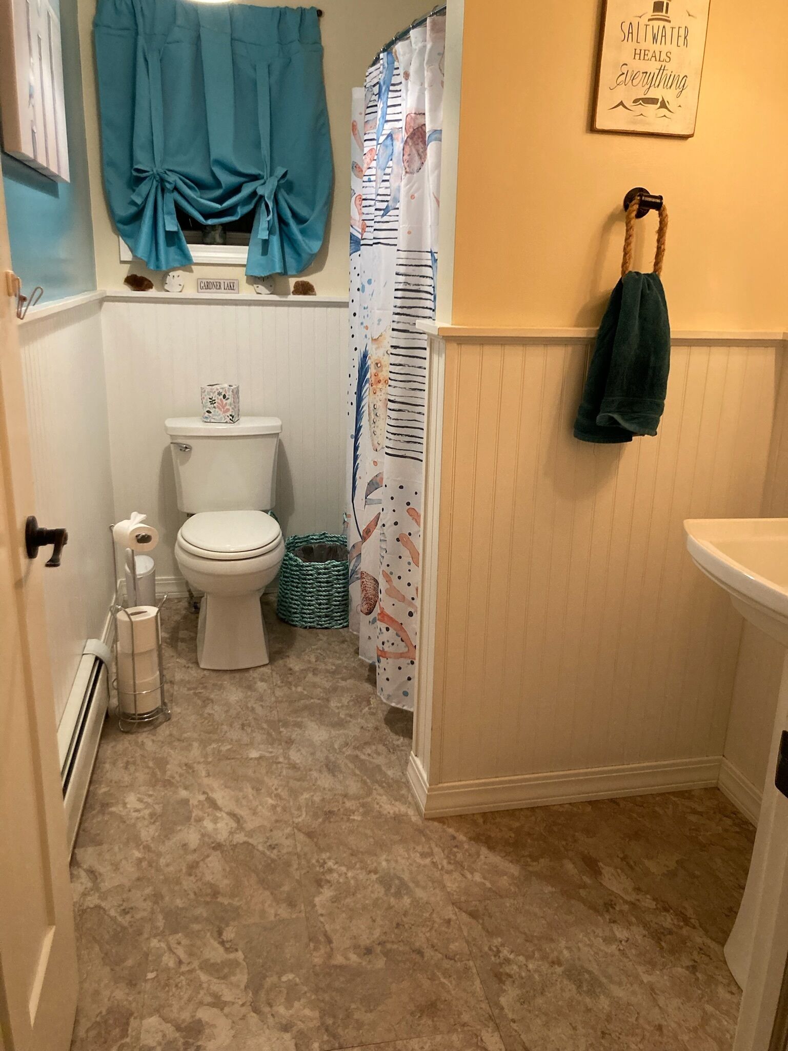 Un bagno con il water, una tenda doccia, un portasciugamani e un cartello appeso al muro.
